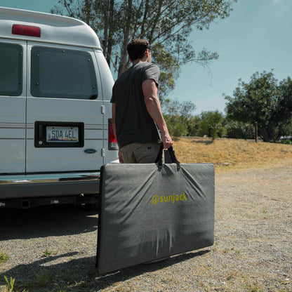 Person carrying SunJack 400 Watt ETFE Foldable Portable Solar Panel Charger near van in outdoor setting.