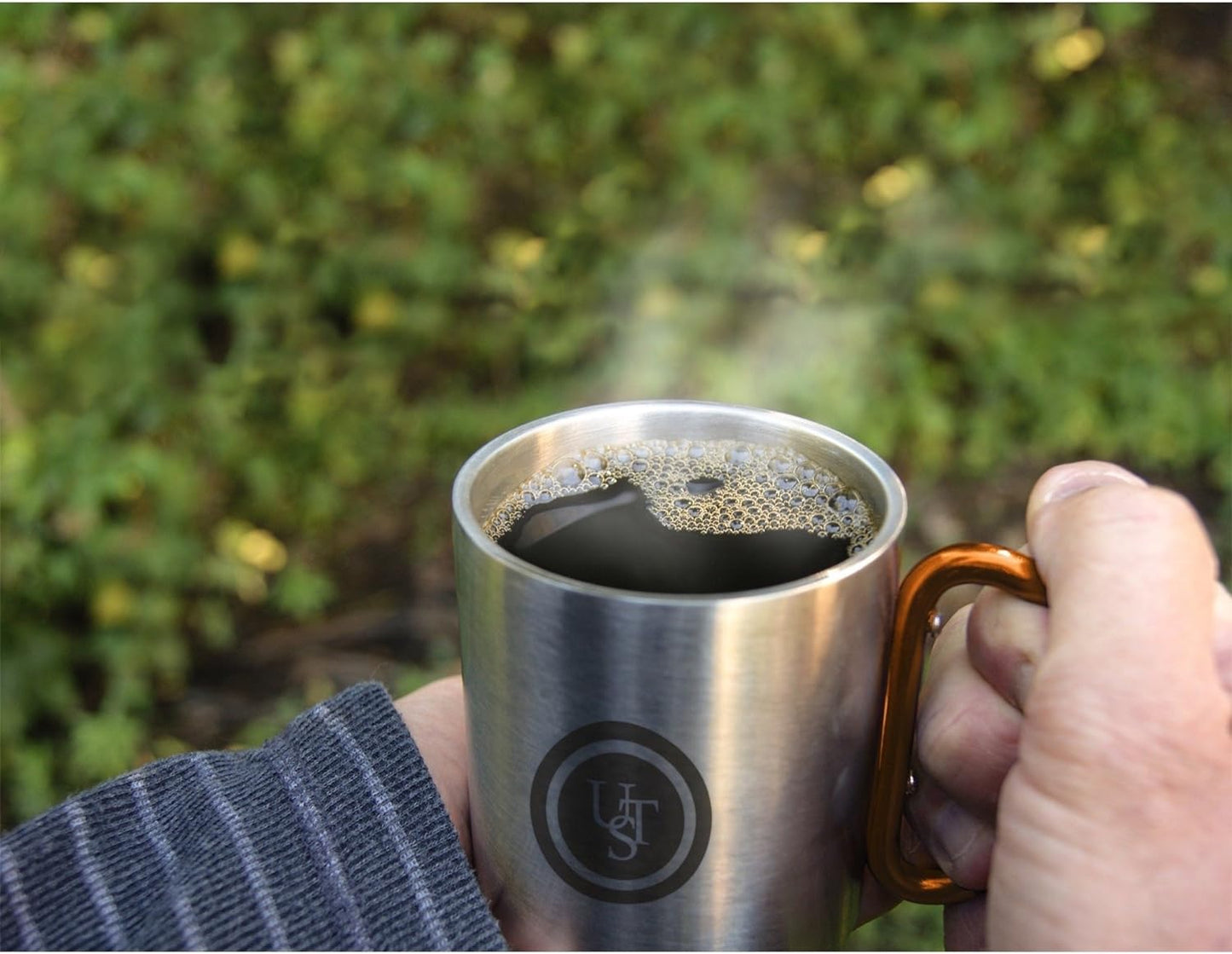 Stainless steel carabiner mug with orange handle in use outdoors.