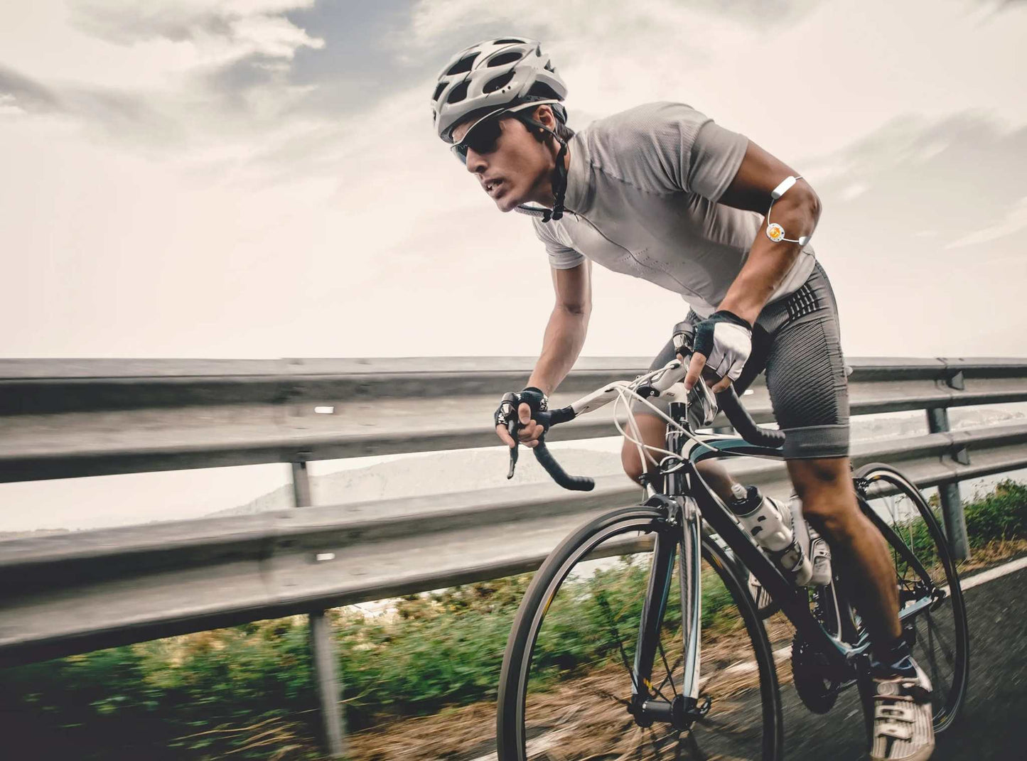 Cyclist using the KT Recovery+ Wave™ wearable device for pain relief during a ride.