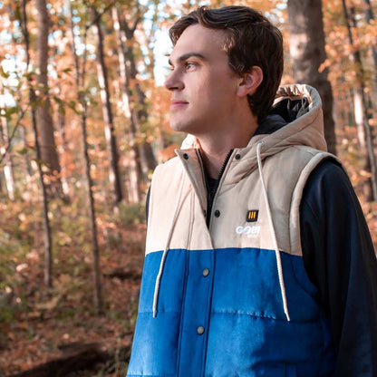 Colt Men's Heated Vest with Hood in deep blue and cream, featuring a drawstring hood and flannel-lined interior, worn by a person in a forest setting.