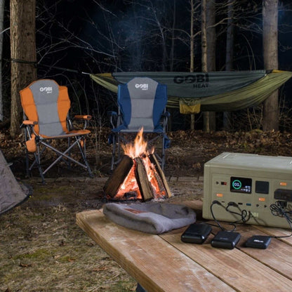 Camping scene with CORE 614W Portable Power Station on a wooden table, powering multiple devices by a campfire.