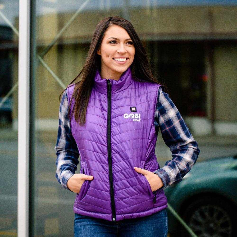 Woman wearing a purple Dune Heated Vest, perfect for staying warm with up to 10 hours of electric heat, in an outdoor setting.