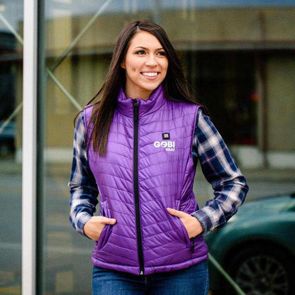 Woman wearing a purple Dune Heated Vest, perfect for staying warm with up to 10 hours of electric heat, in an outdoor setting.