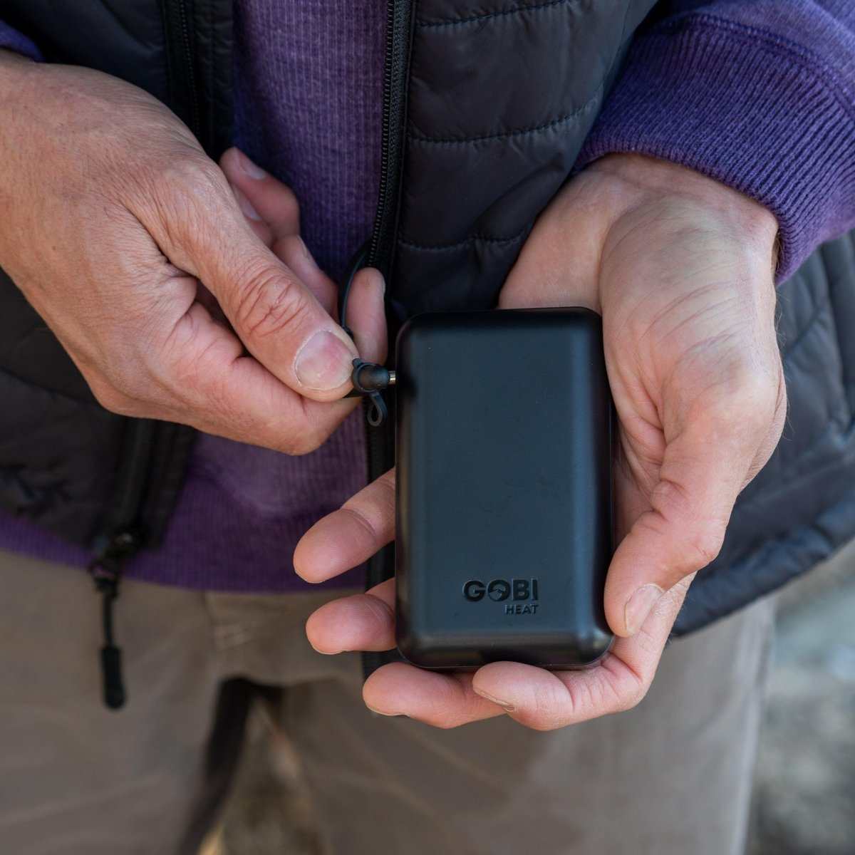 Person holding the compact battery of a Dune Mens Heated Vest.