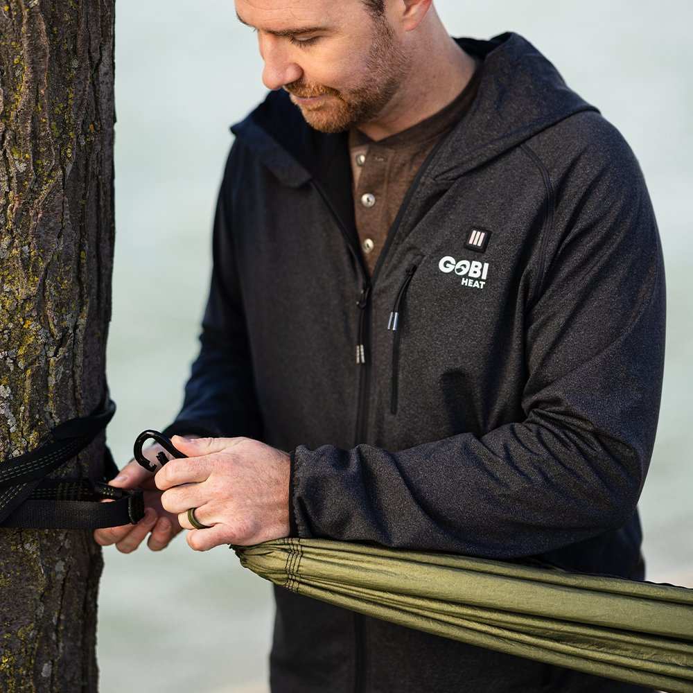 Man setting up an Eclipse Heated Hammock Tent using durable nylon tree straps.