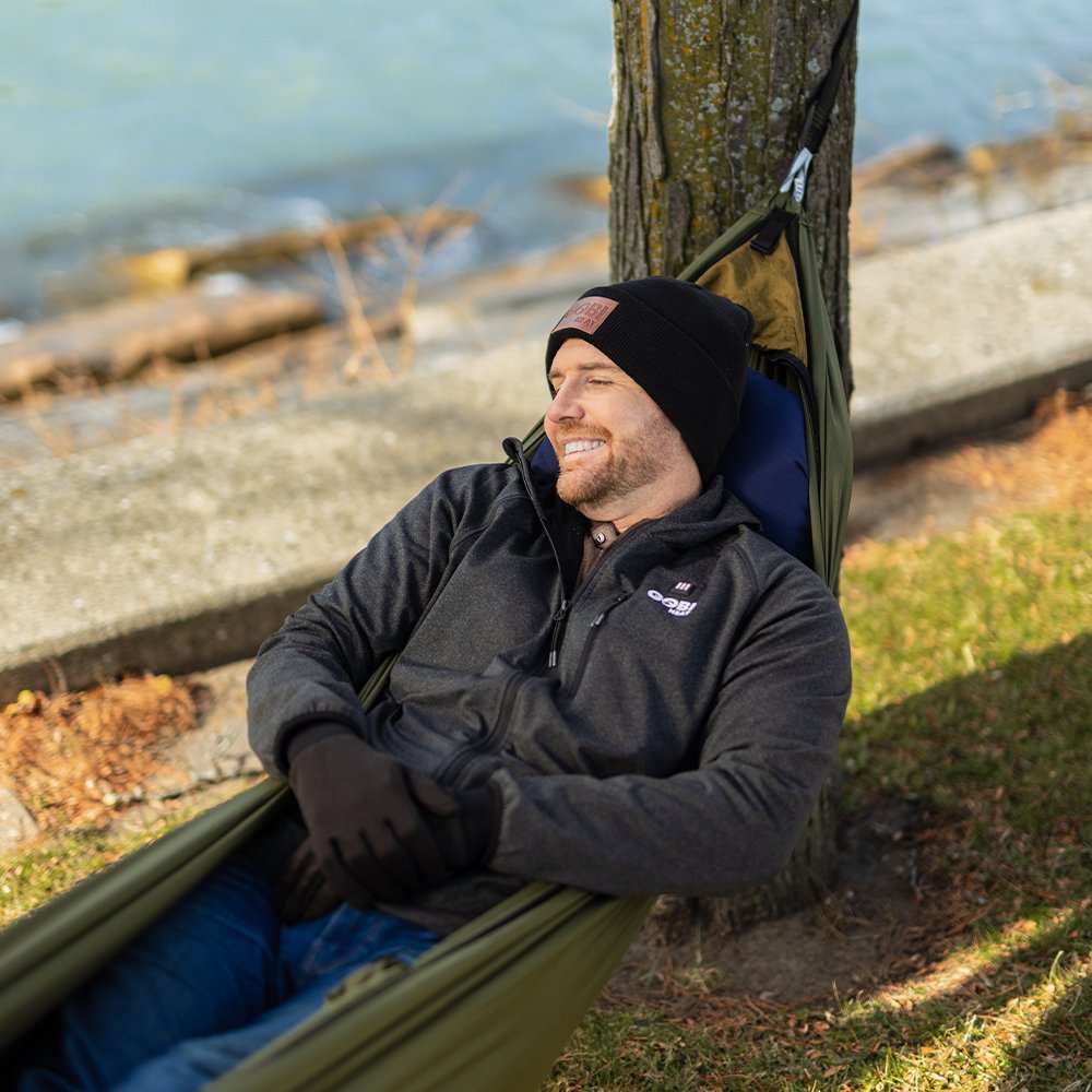 Man relaxing in Eclipse Heated Hammock Tent near a tree by a lakeside.