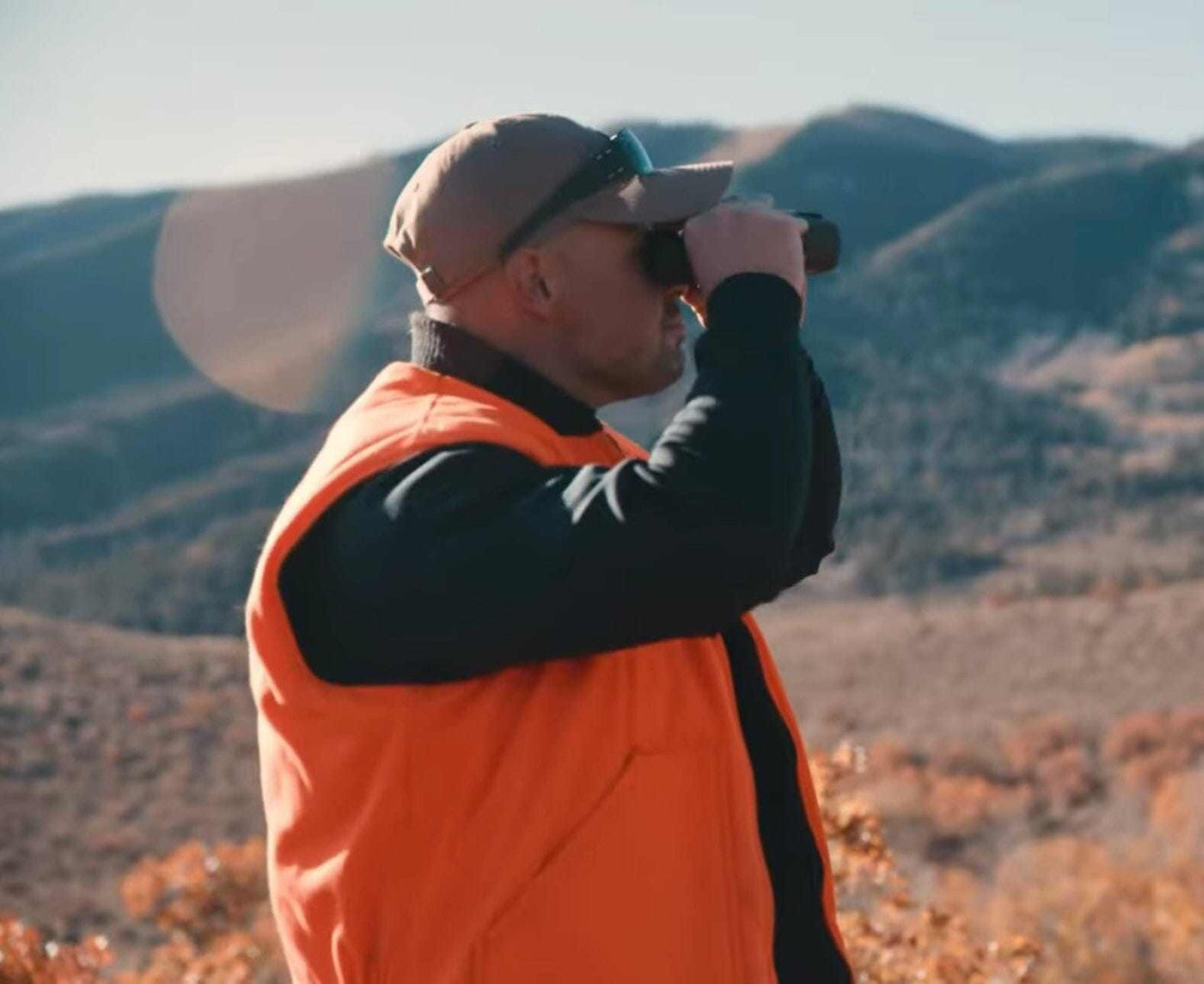 Man wearing Equinoxx K2 Dyna-Thermal shirt and orange vest observes landscape through binoculars.