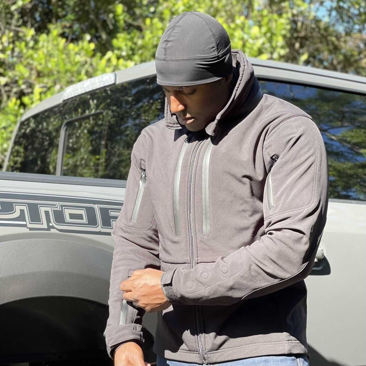 Man wearing a black Equinoxx Watch Cap Beanie outdoors with a truck in the background.