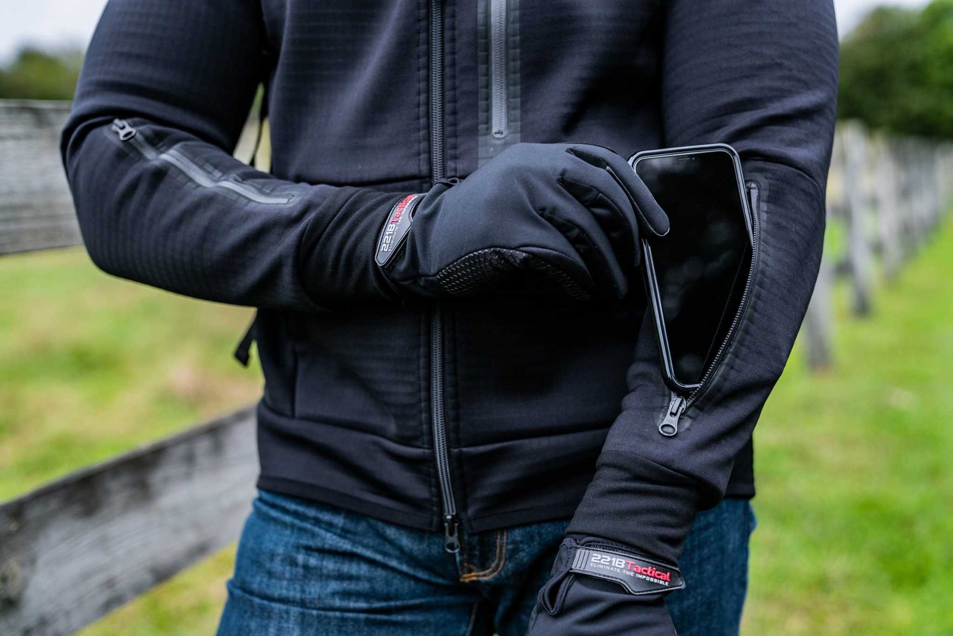 Man wearing Rendition Jacket Elite with waterproof sleeve pocket holding a smartphone outdoors.