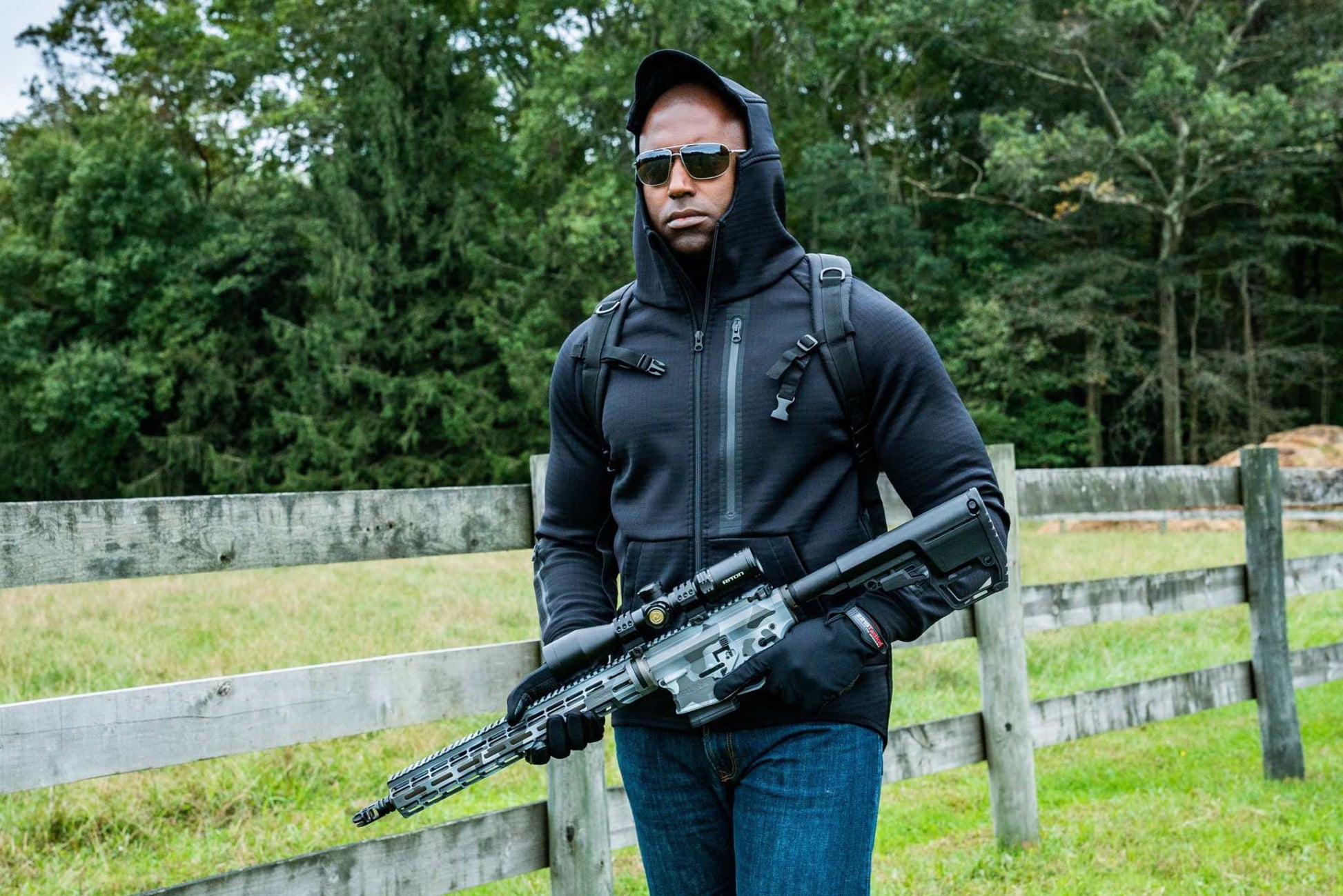 Man wearing Rendition Jacket Elite walking outdoors with a fence and trees in background.