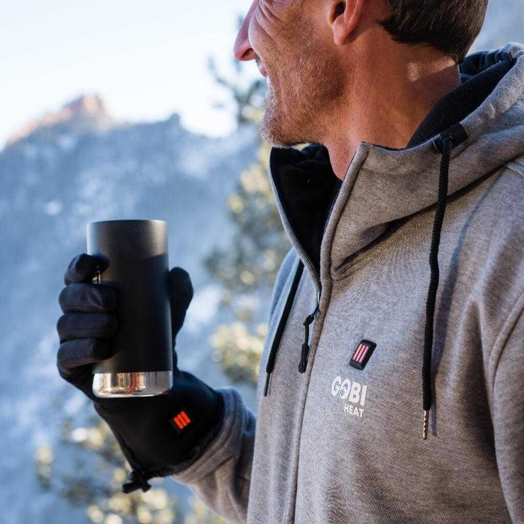 Man wearing Stealth Heated Glove Liners holds a drink, showcasing lightweight and heating features, ideal for outdoor activities.