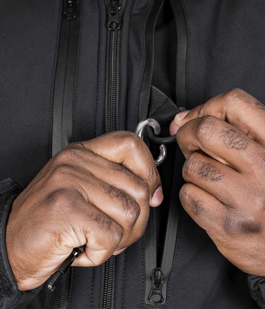 Close-up of hands handling a zipper on the Tradecraft Tactical Jacket 2.0 in black, showcasing waterproof zippers and durable design.