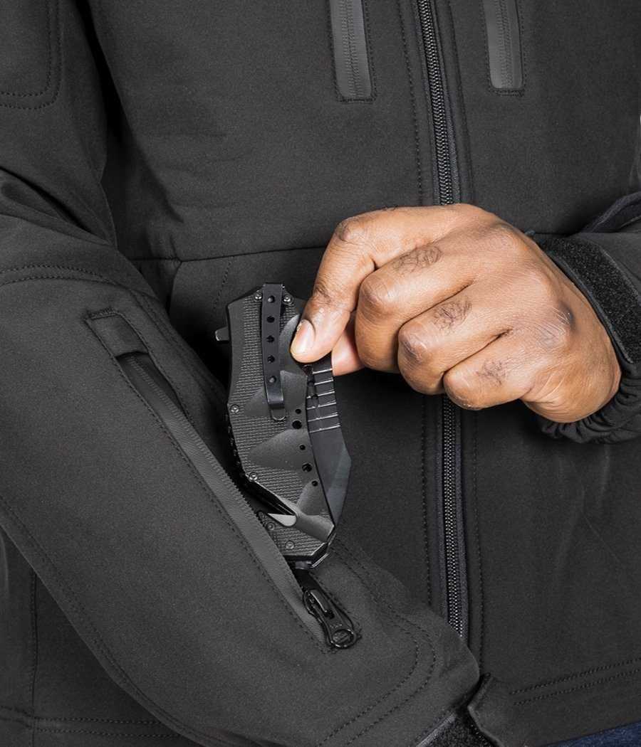 Man accessing knife from pocket of Tradecraft Tactical Jacket 2.0, featuring waterproof zippers and covert storage.