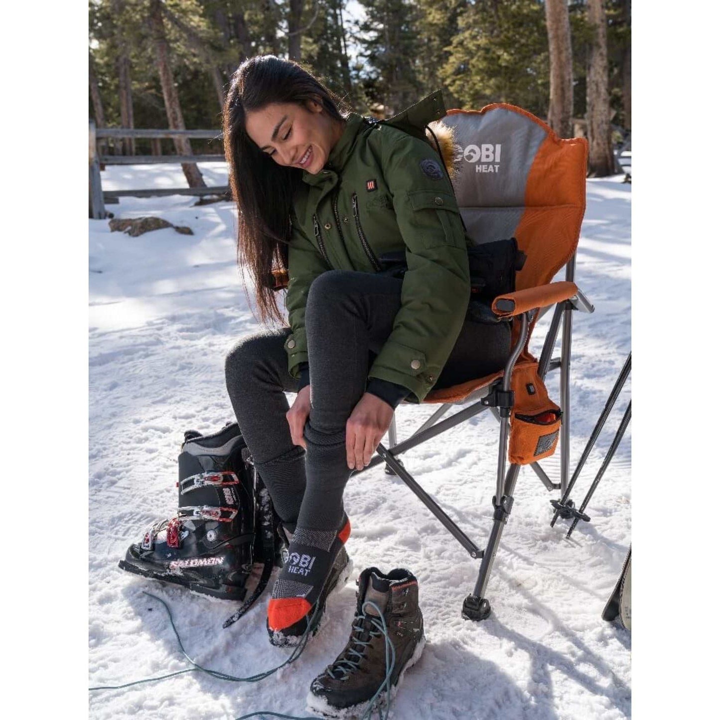 Woman adjusting Tread Heated Socks while sitting in a snowy outdoor setting.