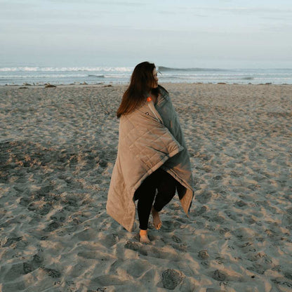 Person wrapped in Zen Portable Heated Blanket standing on the beach.