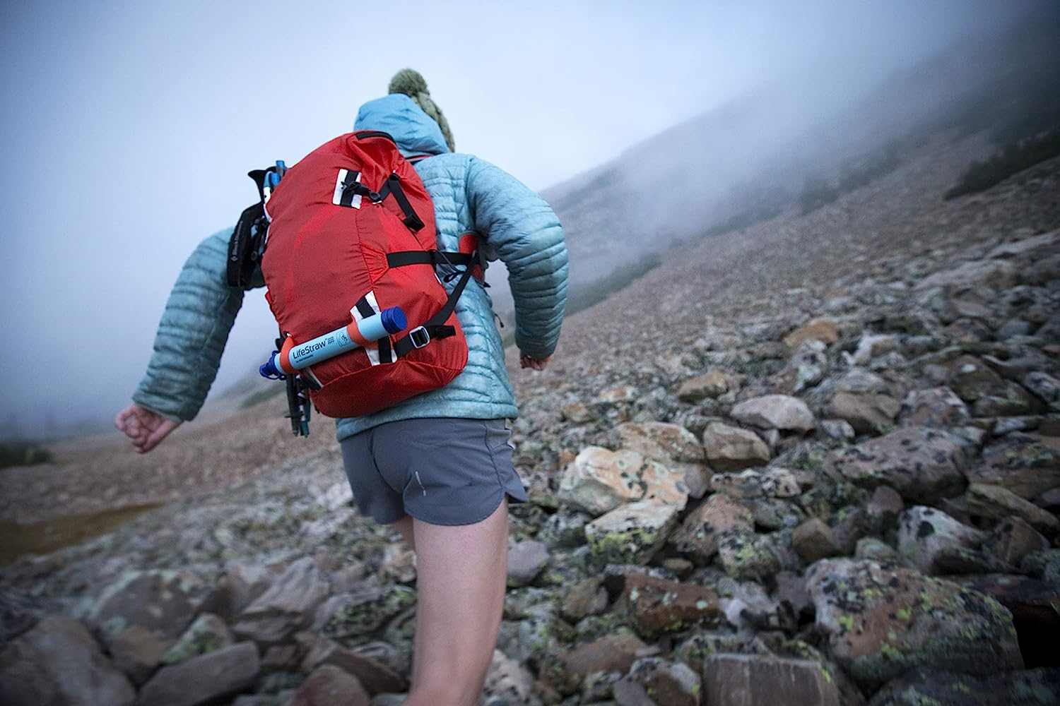 Hiker with red backpack carrying a LifeStraw Personal Water Filter on rocky terrain.