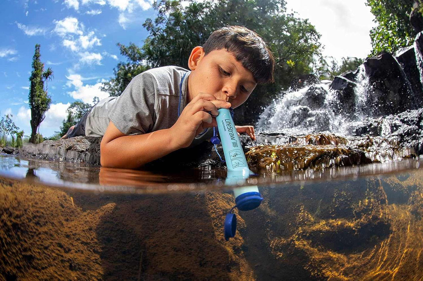 Boy using LifeStraw Personal Water Filter in natural stream.